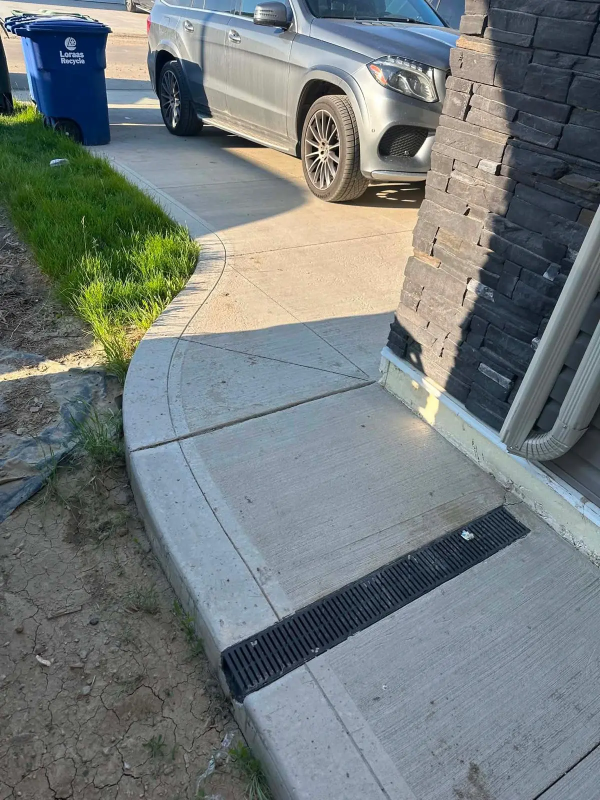 Curved concrete walkway with a grated channel drain beside a Saskatoon home