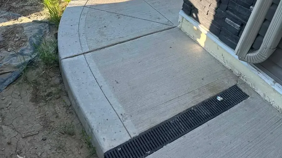 Curved concrete walkway with a grated channel drain beside a Saskatoon home