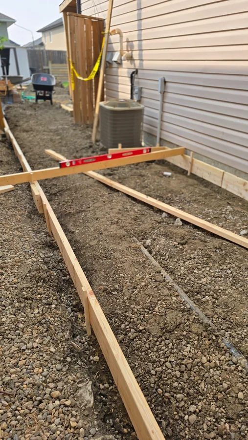 Concrete walkway formwork and base preparation beside a Saskatoon home